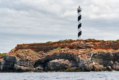 Lighthouse on rock formation by sea against sky