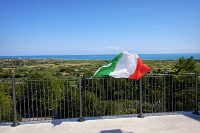 Flag waving on railing against clear sky during sunny day