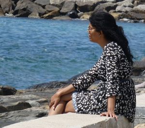 Side view of woman sitting on rock at beach