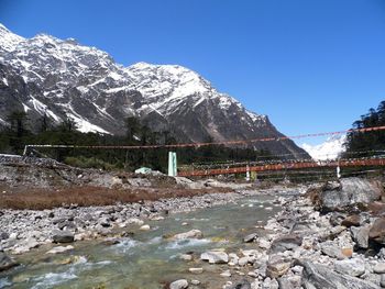 Bridge over teesta river flowing through rocks against clear blue sky at yumthang valley