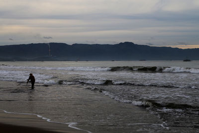 Silhouette man standing on beach against sky during sunset