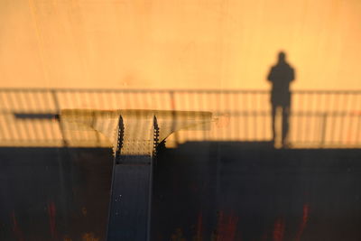Silhouette man standing by railing against orange sky