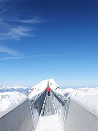 Rear view of people walking on footbridge at snow covered mountains against sky