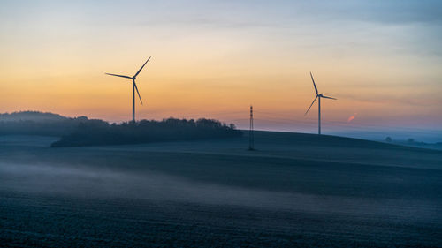 Wind turbines on field against sky during sunset