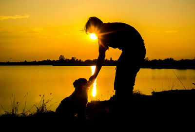 Silhouette people by lake against sky during sunset