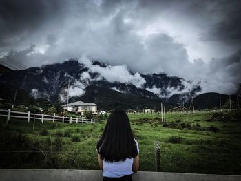 Rear view of woman standing on mountain against storm clouds