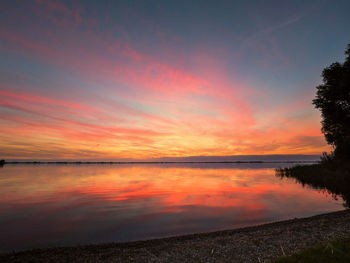 Scenic view of calm lake against dramatic sky during sunset