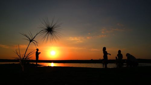 Silhouette people on beach against sky during sunset