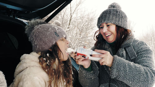 Winter tea picnic, outdoors. happy child is eating whipped cream from a spray, tube. 
