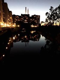 Silhouette buildings by lake against sky in city at night