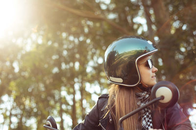 Young woman in helmet riding motorcycle on sunny day