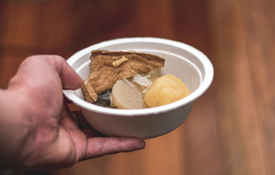 Close-up of hand holding food in bowl on table