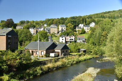 Houses by river and buildings against clear blue sky