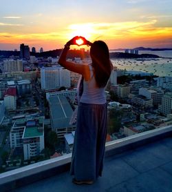 Rear view of woman gesturing against sky during sunset