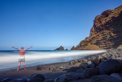 Rear view of rocks at beach against clear blue sky