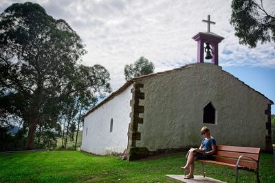 Woman reading book while sitting against church