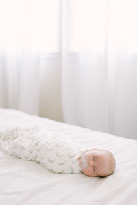 Newborn sleeping swaddled in a rainbow blanket on white bed