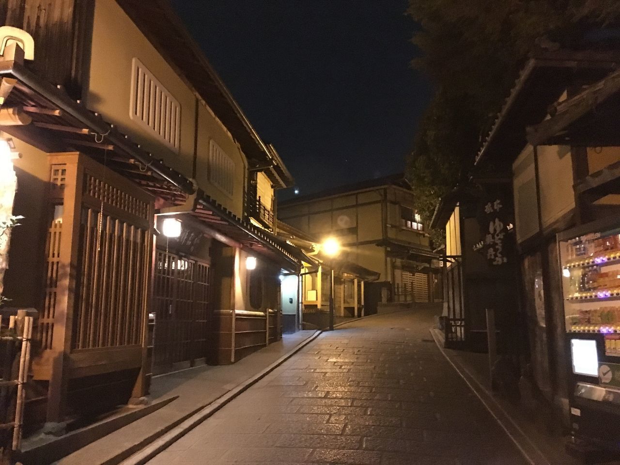 EMPTY STREET AMIDST ILLUMINATED BUILDINGS AT NIGHT