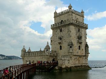 View of historic building by sea against cloudy sky