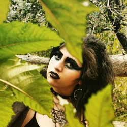 Portrait of woman with make-up seen through leaves in forest