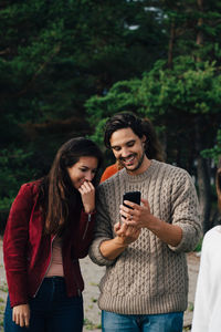 Happy young woman photographing while using smart phone