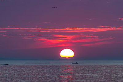 The bright sun rising above lighthouse and fisherman in the ocean.