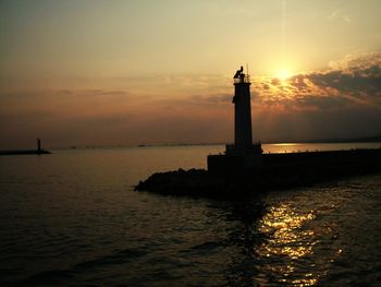 Lighthouse by sea against sky during sunset