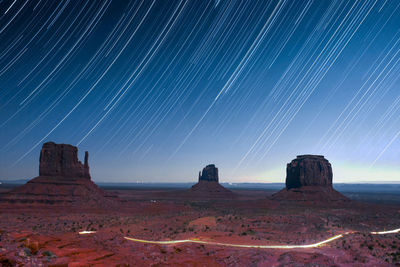 Scenic view of monument valley against star trails against sky at night