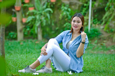 Portrait of smiling young woman sitting on land in park