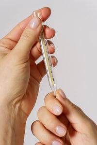 Close-up of hand holding thermometer against white background