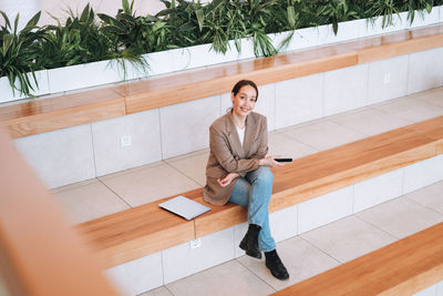 Adult smiling brunette business woman in beige suit and jeans working on laptop at public place