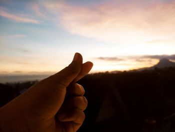 Cropped hand of woman holding heart shape against sky during sunset