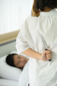 Midsection of woman holding white while standing on bed