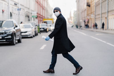 Side view of man wearing mask crossing road in city