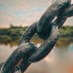 Close-up of rusty metal chain against sky during sunset