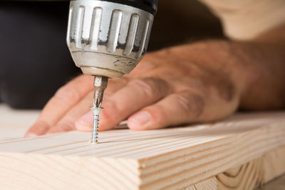 Cropped hand of man drilling wood at home