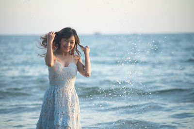 Portrait of smiling woman standing in sea against sky