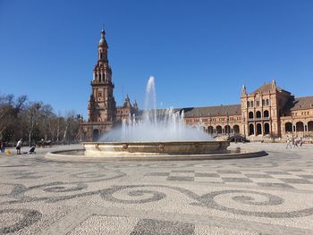 Fountain in front of historic building against clear sky