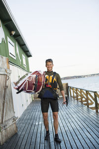 Full length portrait of happy man carrying kayak on shoulder at boathouse