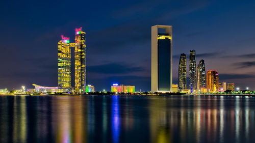 Illuminated city by river against sky at night