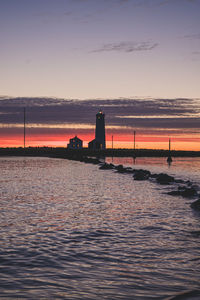 Lighthouse by sea against sky during sunset