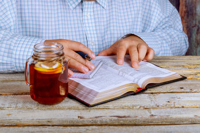 Close-up of man holding book by drink on table