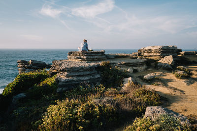 Woman sitting on rock by sea against sky