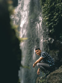 Full length portrait of young on on rock with waterfall in the background