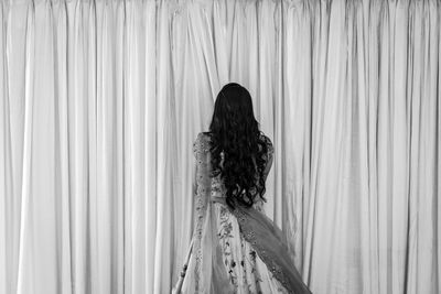 Rear view of woman standing against curtain