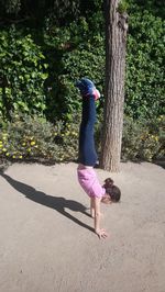 Girl doing handstand on footpath against plants