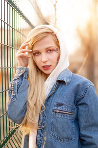 Portrait of beautiful young woman standing by fence