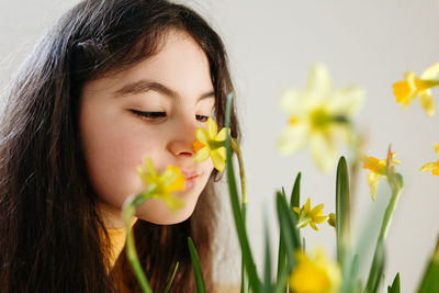 Close up portrait of dark haired child watching yellow daffodil flowers