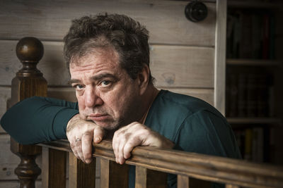 Portrait of man leaning on wooden railing at home