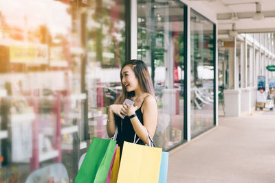 Young woman with shopping bags standing outside store